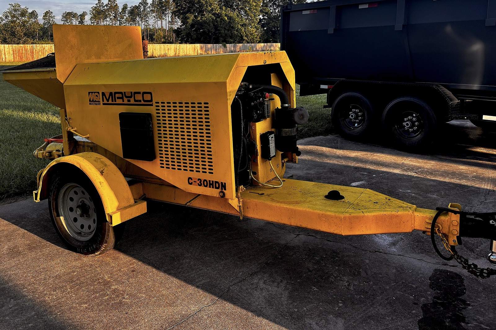 Yellow Mayco C-30HDN trailer-mounted concrete pump parked on a concrete driveway in evening light.